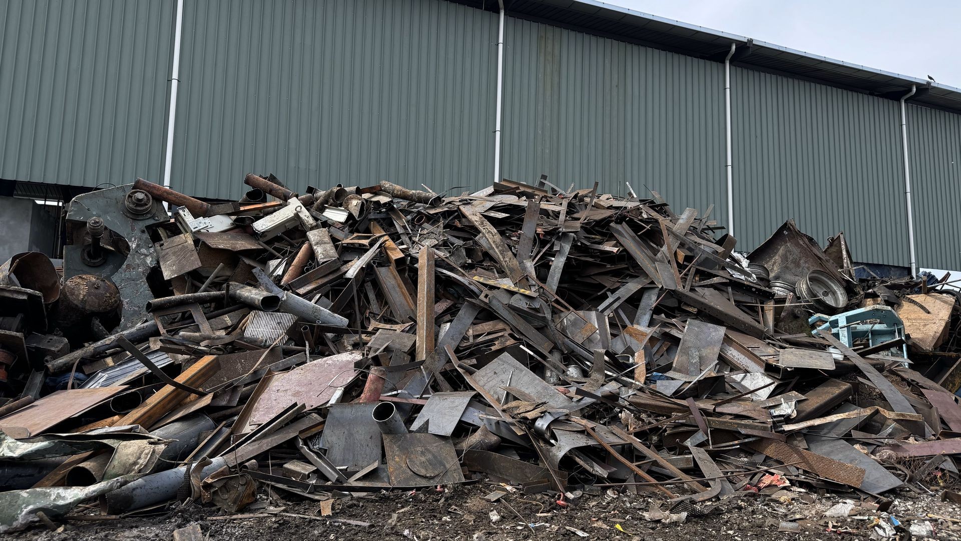 Large pile of scrap metal and debris piled up in front of a grey industrial building.